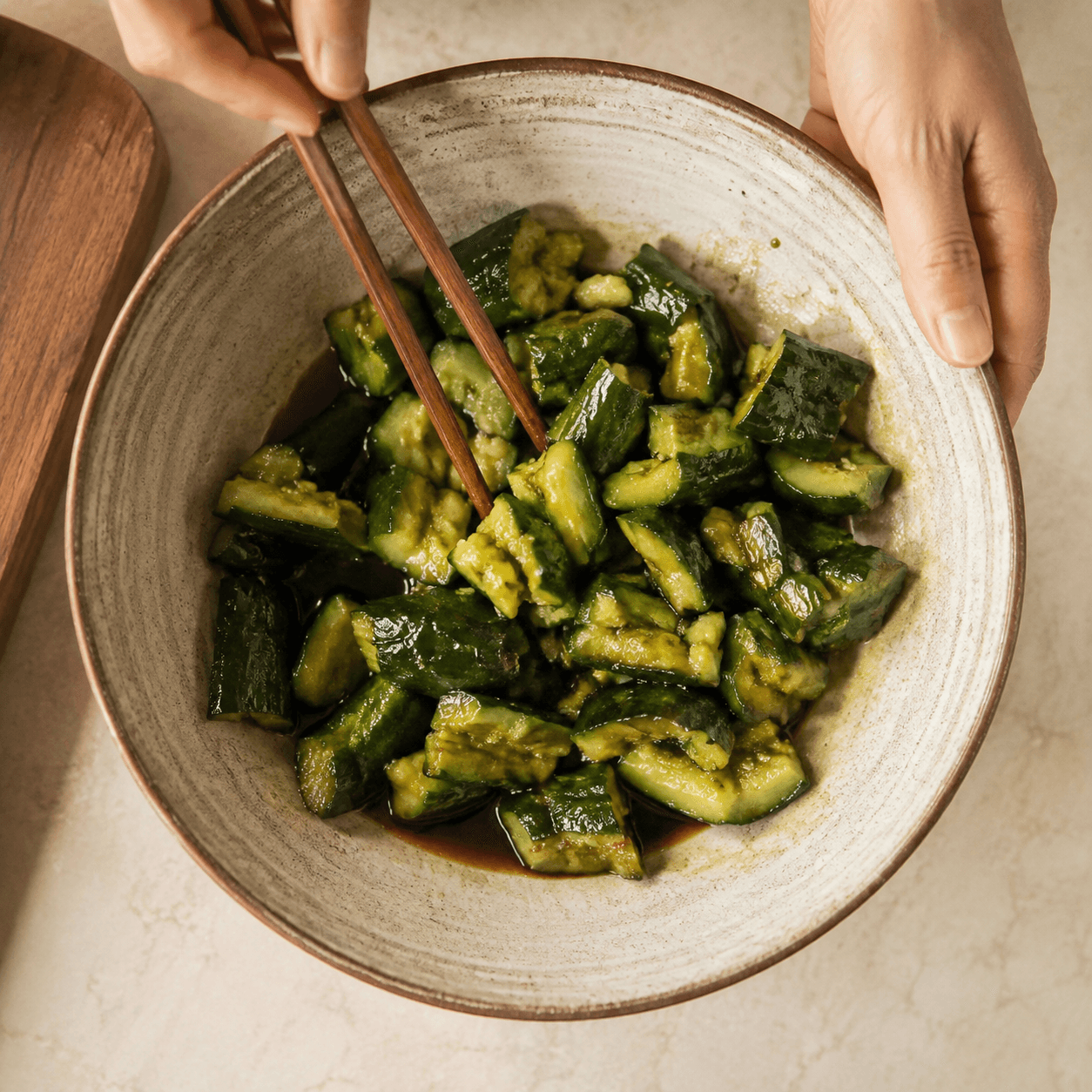 Smashed cucumber pieces tossed with a glossy dressing until evenly coated in a bowl.