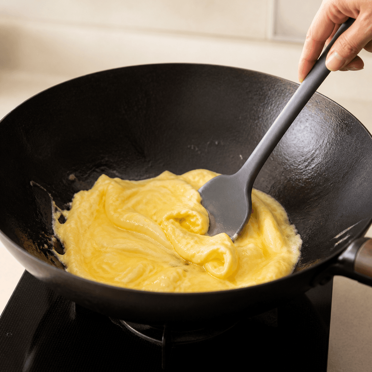 Eggs just set into glossy pale ribbons in a wok, pushed by a spatula.