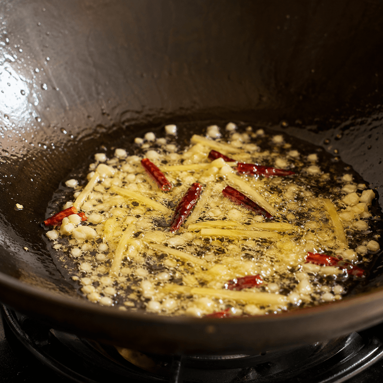 Minced garlic, ginger slivers and dried chilies sizzling in shallow oil at the edge of a wok.