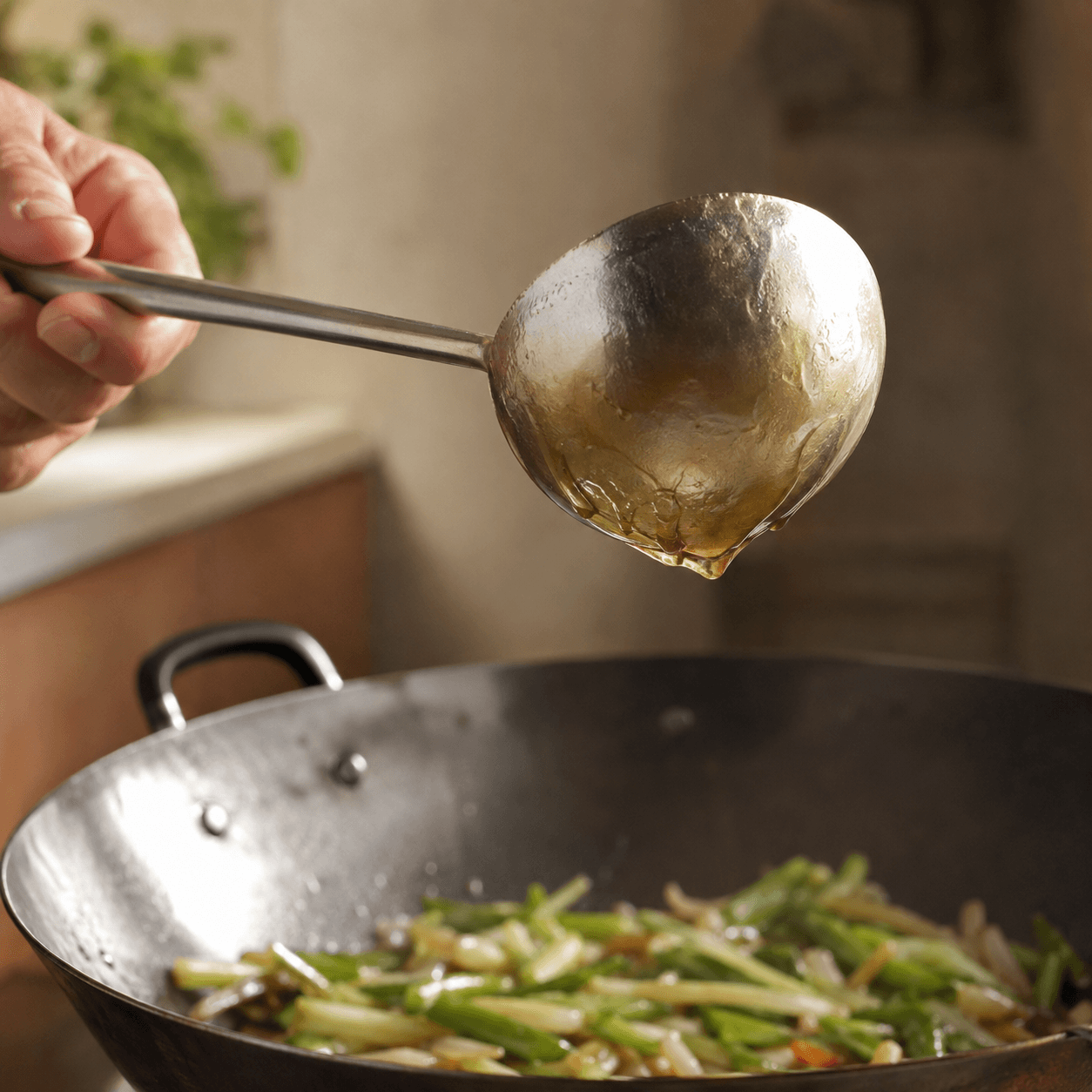 Glossy sauce lightly coating the back of a ladle lifted from a wok.